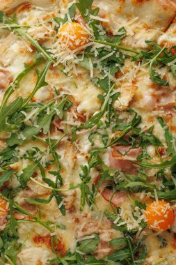 Taze bir pizza roka, peynir ve portakallı domatesle kaplıdır. İnsanlar akşam yemeği için bir restoranda masanın etrafında toplanıyorlar. Atmosfer canlı ve parlak..