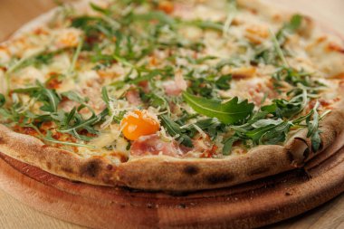 Erimiş peynir, biraz jambon ve çeşitli taze roka içeren yuvarlak bir pizza tahtanın üzerine yerleştirilir. Ortam sıcak ve davetkar. Yemek için mükemmel..