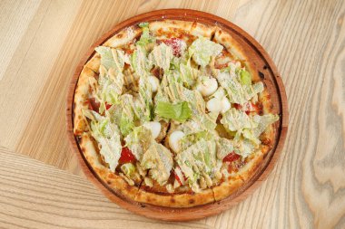 Yuvarlak bir pizza marul, domates ve bir tutam peynirle kaplıdır. Tahta bir tabakta sunuluyor. Ayar hafif ahşap yüzeylere sahiptir..