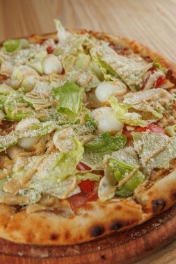 Ahşap tabaklarda uluslararası bir tabak seçimi sergilenmektedir. Üzerinde marul, domates ve soğan bulunan pizza, canlı renkler ve taze malzemeler sergileniyor..