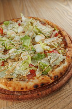 Yeni pişmiş bir pizza ahşap servis tahtasına yerleştirilir. Pizza dilimlenmiş marul, domates ve peynirle kaplı, öğle yemeği veya akşam yemeği için hazır..