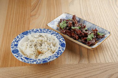 Bir kase buharda pişmiş pirinç, otlar ve tohumlarla süslenmiş bir tabak kızarmış etle eşleştirilir. Bu yemek Asya mutfağının tadını gösteriyor..