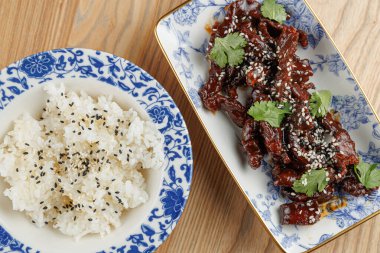 Otlarla süslenmiş lezzetli bir tabak et susam tohumlarıyla süslenmiş bir kase kabarık beyaz pirincin yanında oturur. Bu, lezzetli bir yemek için kültürel mutfakların karışımını sergiliyor..