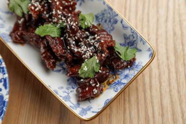 Dekoratif bir tabakta proteinler ve süslemeler yer alır. Sunumda çeşitli uluslararası mutfak etkileri sergileniyor ve bu da keyif vermeye teşvik ediyor..