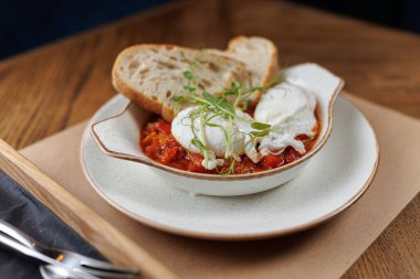 Bir tabakta lezzetli bir sosa konmuş iki haşlanmış yumurta ve taze ekmek dilimleri var. Sahne, sıcak bir atmosferdeki basit bir yemeği yakalar..