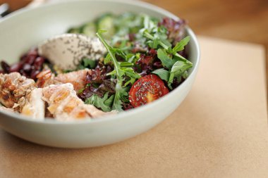 Cömert bir porsiyon taze salata, ızgara tavuk, kiraz domatesleri, karışık sebzeler ve bir tutam sos. Bu canlı yemek, öğleden sonra bir kafede servis edilir..