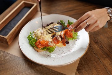 Somon, yeşillik ve ekmek içeren bir tabağı keserken bir el çatal ve bıçağı tutar. Ortam rahat ve rahat, arkadaşlarla ya da aileyle öğle yemeği için uygun..