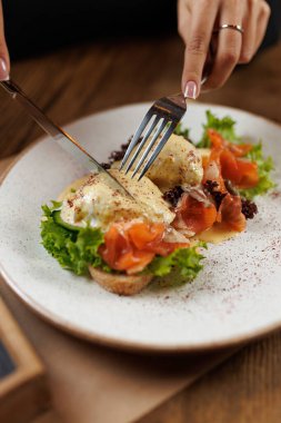 Taze yeşilliklerle çevrili, haşlanmış yumurtalarla kaplı, füme somonlu brunch tabağından hoşlanan bir insan. Çatal ve bıçak çalışıyor, ısırmaya hazır..