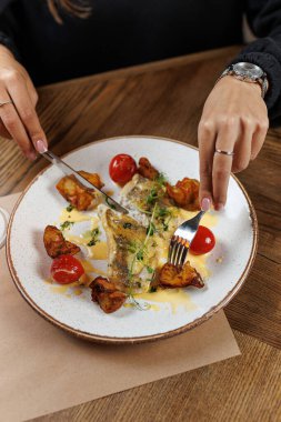 Bir insan kızarmış patates ve vişneli domatesle bir tabak balık yemeye hazırlanıyor. Ayar, ahşap bir masa ve basit bir tabak tasarımı içeriyor..