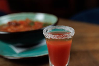 Farklı mutfaklardan leziz bir yemek dizisi, ferahlatıcı bir içeceğin yanında sergileniyor. İçecekte tuzlu bir kenar ve canlı renkler var. Bu da yemek deneyimini arttırıyor..