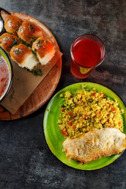 Renkli bir yiyecek çeşidi arasında baharatlı pirinç, ızgara balık, yumuşak ekmek ruloları ve bir içecek yer alıyor. Yemekler ahşap bir masada farklı kültürler ve tatlar sergiliyor..