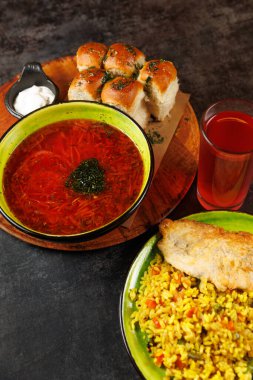 Yumuşak ekmek ruloları ve ahşap tabakta sarı pirinçli ızgara balığın eşlik ettiği, üzerinde otlar bulunan bir kase kırmızı borş afiyetle yiyin. Bir bardak kırmızı içecek yemeği tamamlar..