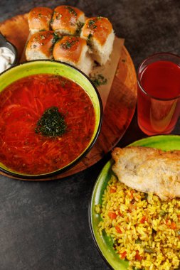 Ukrayna borş çorbası, otlar, kızarmış balıklar, renkli pirinç, yumuşak ekmek ruloları ve kırsal ahşap bir masaya kurulmuş bir bardak içki içeren çeşitli bir yiyecek yayılımı..