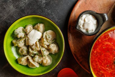 Hamur köfteleri ekşi kremayla kaplı yeşil bir kaseye konur. Tahta bir yüzeyde bir kase çorba bulunuyor. Yemekler geleneksel Ukrayna yemeklerini gösteriyor.