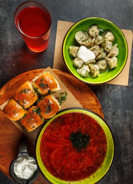 Bir masada geleneksel Ukrayna yemekleri sergilenirken, bir kase sebzeli borş, bir tabak hamur köftesi ve ekmek ruloları yer. Bir içki yakınlarda oturur, yemeği tamamlar..