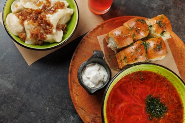 Çeşitli geleneksel yemekler ahşap bir tabakta düzenlenir. Üstünde soğan, bir kase kırmızı çorba ve yumuşak ekmek ruloları olan hamur tatlısı var. Bu sahne zengin bir mutfak deneyimini yakalar..