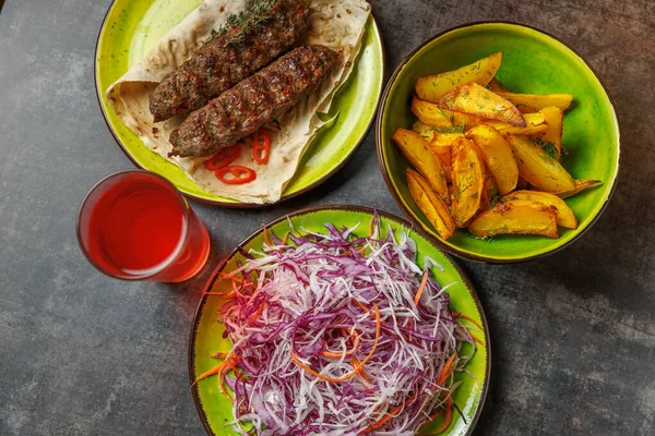 Patates ve salatayla servis edilen kebap tabakları. Yakınlarda bir bardak içki var. Bu yemek, canlı bir yemek atmosferinde değişik lezzet ve kültürler sergiliyor..