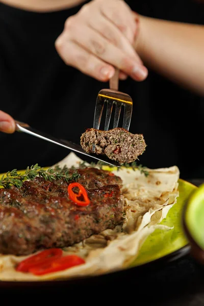 Bir insan masada otururken bir çatalla Ukrayna et tabağından bir dilim alır. Tabak taze otlar ve biberlerle süslenir, sıcak ekmek üzerine konur..