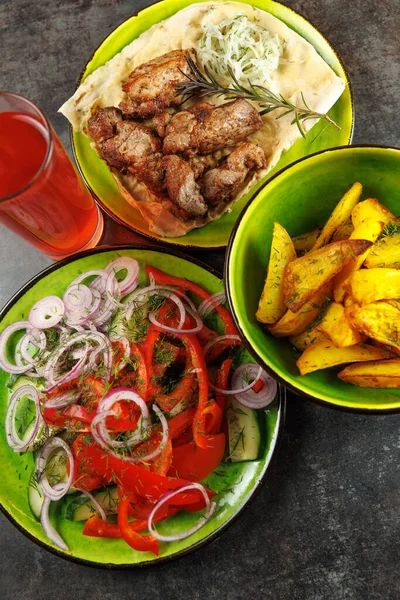 Taze hazırlanmış yemekler: Kızarmış et, baharatlı patates ve renkli bir salata. Bu yemek farklı kültürlerden aşçılık gelenekleri sergiliyor ve harika bir yemek deneyimi sunuyor..