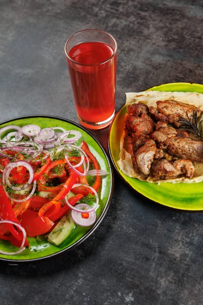 Kızarmış et, salata, salata, domates ve soğandan yapılmış. Tabakların yanında bir bardak kırmızı içecek rengarenk yemekler hazırlıyor..