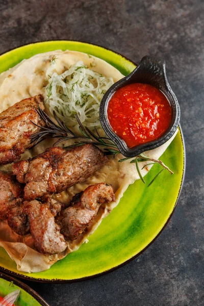 Bir porsiyon ızgara et taze salata ve küçük bir kase kırmızı sosla birlikte yeşil bir tabakta sunulur. Bu yemek çeşitli mutfaklardan oluşan çeşitli bir yemeğin parçasıdır..