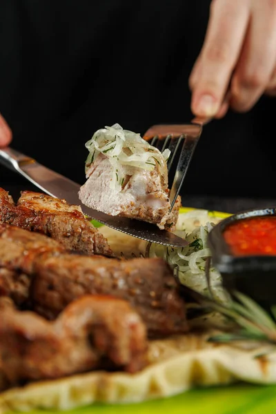 Lezzetli kızarmış et dilimlenir ve soğanla süslenir. Bir insan eti servis etmek için çatal ve bıçak kullanıyor. Tabak, yanında sos olan ahşap bir tabakta sunuluyor..