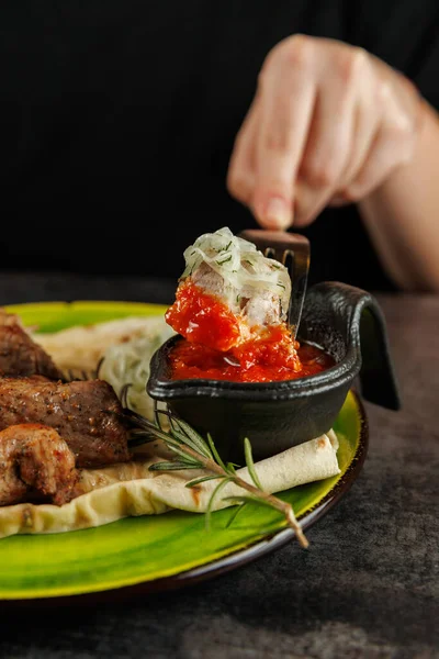 Bir tabak Ukrayna et yemeklerinin yanında taze malzemelerle hazırlanmış Japon yemekleri içerir. Bir el, masayı sosa batırır..