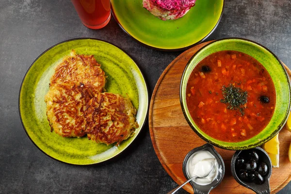 Bir masada, tabakta patatesli gözleme, tabakta kırmızı borş sosu ve yanında tat vermesi için ekşi krema ve zeytin gibi malzemeler bulunan doyurucu Ukrayna mutfağı sergileniyor..