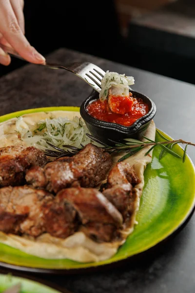 Bir el, bir tabak soğanlı ve bir kase kırmızı soslu ızgara et için uzanır. Yemek, canlı bir yemek ortamında lezzetlerin kültürel bir karışımını sergiliyor..