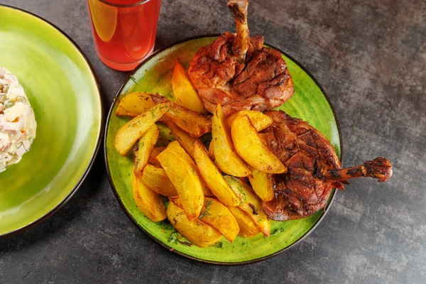 Açık yeşil bir tabakta kızarmış tavuk budu ve çıtır patates dilimleri servis edilen bir yemek. Yakınlarda renkli bir içecek duruyor, ziyafete renk katıyor..