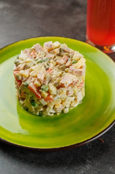 Geleneksel bir Ukrayna yemeği parlak yeşil bir tabak üzerinde düzgün bir yığın halinde sıralanmış renkli sebze ve et karışımına sahiptir. Arka planda bir içecek görünüyor..