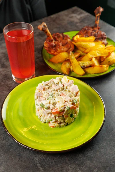 Bir yemek vitrininde sebze ve etten yapılmış bir Ukrayna salatası, yanında kızarmış tavuk parçaları, patates parçaları ve kırmızı bir içecek var. Ayar gündelik ve davetkar..