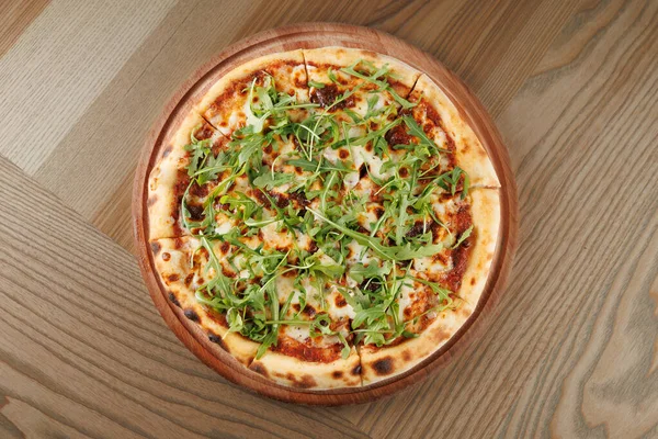Yuvarlak bir pizza, taze yeşillik ve peynirle kaplı ahşap bir tahtanın üzerinde duruyor. Bu yemek sıradan bir toplantıda paylaşmak için mükemmel bir lezzet karışımını temsil ediyor..
