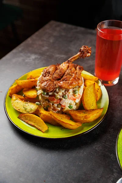 Tabakta çıtır tavuk ve iyi pişmiş patates parçaları var. Tabağın yanında, bir bardak kırmızı içecek yemeği tamamlar. Ayar gündelik ve davetkar..