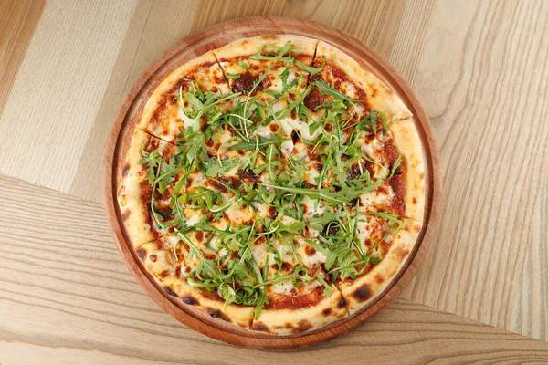 Altın hamurlu yuvarlak bir pizza erimiş peynir ve zengin domates sosu içerir. Kırsal ahşap bir tabakta taze roka ile cömertçe süslenmiştir..