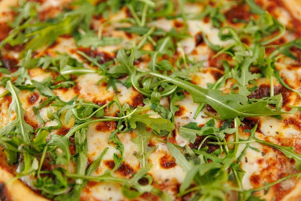 Taze pişmiş bir pizza erimiş peynir ve canlı roka yapraklarıyla kaplıdır. Bu yemek bir ev mutfağında pizza yapma sanatını sergiliyor..