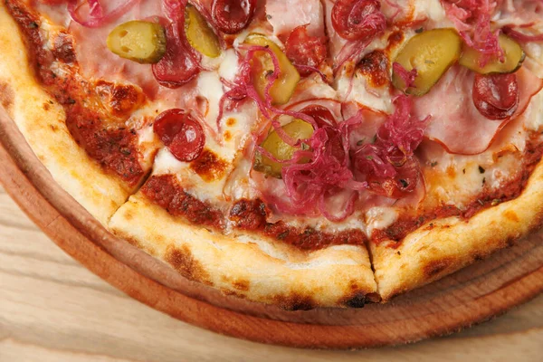 Bir grup, jambon, turşu, domates ve soğan gibi malzemelerle pizza yemek için ahşap bir masanın etrafında toplanıyor. Ortalık sakin ve davetkar. Birlikte yemek için mükemmel..