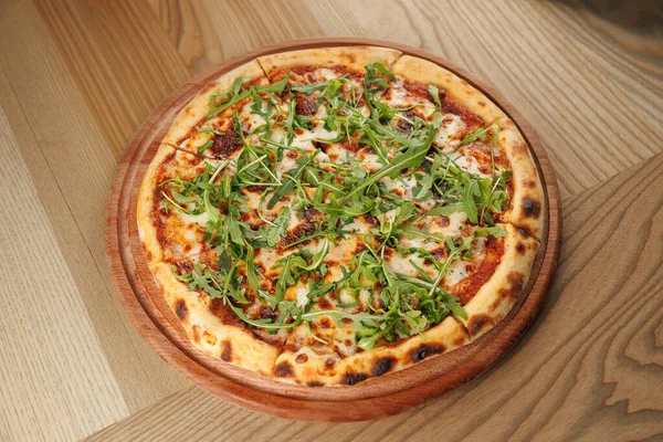 Eritilmiş peynir, kırmızı sos ve taze roka ile kaplı yuvarlak bir pizza sıradan bir restorandaki ahşap bir tahtanın üzerine yerleştirilir. Samimi bir ortamda İtalyan mutfağının tadını çıkarıyorum..