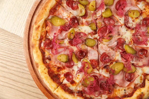 Katmanları jambon, turşu ve soğanlı bir pizza yuvarlak ahşap bir tabakta sunulur. Yemek çeşitli malzemeler sunuyor. İştahı davet ediyor..