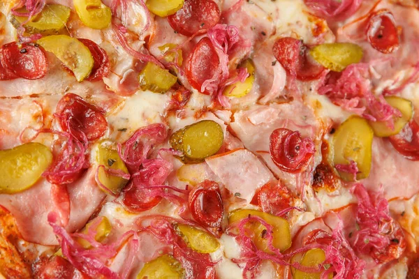 Bir tabak, üzerinde jambon, turşu ve soğan bulunan yeni pişmiş bir pizza içeriyor. Renkli malzemeler, sıradan bir yemek ortamında altın bir kabuk üzerinde sergileniyor..