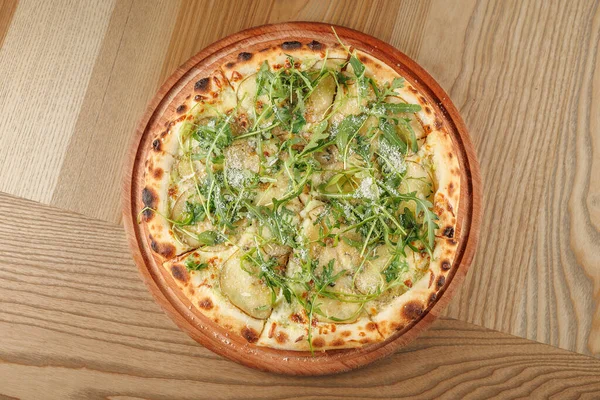 Pizza taze sebzeler, dilimlenmiş sebzeler ve rendelenmiş peynirle kaplı ince bir kabuğa sahiptir. Ahşap aksanlı bir restoranın tahta tahtasında servis ediliyor..