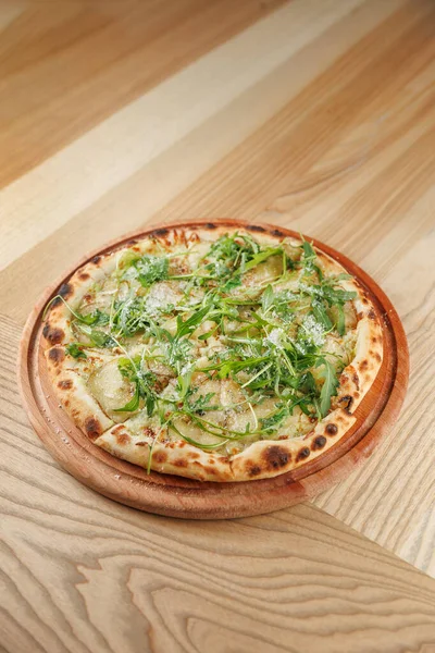 Tahta bir tepside taze roka ve çeşitli otlarla kaplı bir düz ekmekli pizza. Kabuğu altın gibi kahverengi ve çıtır çıtır. Sıradan bir yemek ortamında tadını çıkarmaya hazır..