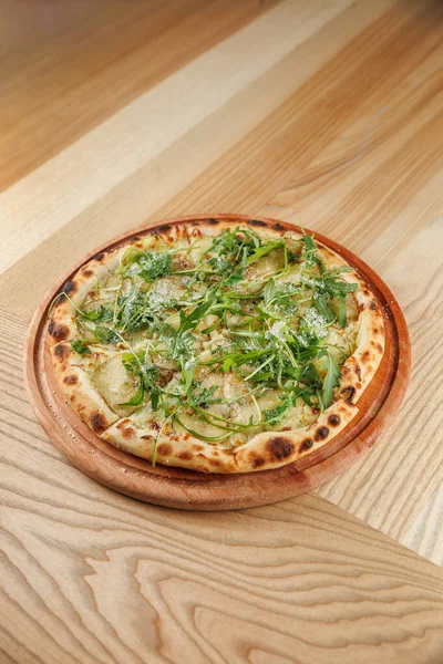 Tahta servis tahtasında taze yeşillikle kaplanmış ahşap kaplı pizza sunuluyor. Bu yemek basit malzemeler sergiliyor ve sıradan bir yemek deneyiminin parçası..