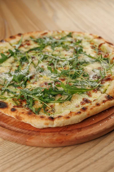 Taze roka ve erimiş peynirle kaplı bir ekmek ahşap bir tahtanın üzerinde duruyor. Ayarlar, rahat bir ortamda keyifli bir yemek olduğunu gösteriyor..