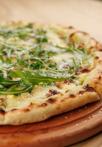 Yuvarlak bir pizza tahta bir tahtaya yerleştirilir. Pizzanın altın bir kabuğu var ve üzeri taze roka ve rendelenmiş peynirle kaplı. Lezzet ve dokuların karışımını sergiliyor..