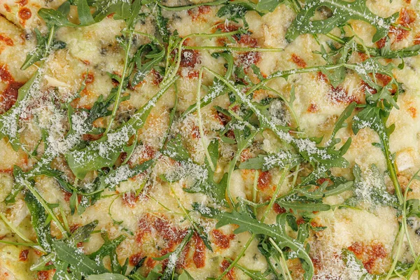 Taze pizza, erimiş peynir ve canlı roka ile kaplı bir masada oturur. Tabakta kabuklu bir taban sergileniyor ve içinde çeşitli tatlar var. Herkesi bir lokma yemeye davet eder..