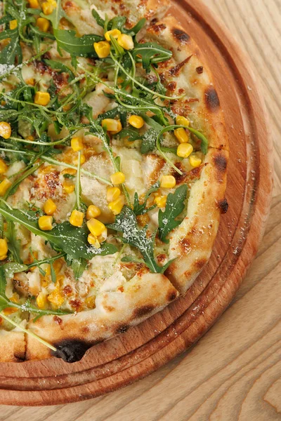 Taze pizza yuvarlak bir ahşap tahtada sergilenir. Ekmek altın ve kıtır kıtır, üstü roka ve tatlı mısırla kaplı, sıradan bir yemek yerinde eğlenmeye hazır..