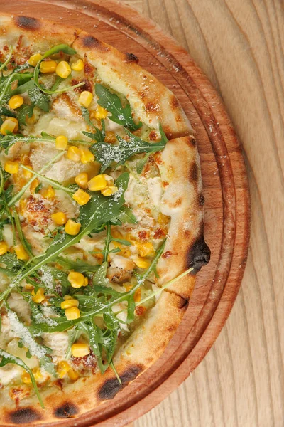 İnsanlar taze pişmiş bir pizzayı paylaşmak için bir masanın etrafında toplanırlar. Pizzada tatlı mısır ve taze roka var. Sıcak, davetkar atmosfer güzel anları teşvik eder..