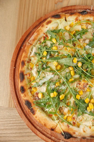 Çeşitli mutfaklardan seçilen yiyecek parçaları ahşap bir masada sergilenmektedir. Tabaklar içinde mısır ve sebzeli pizza da var. Taze malzemeler her tabakta görünür..