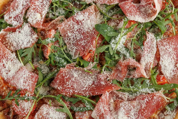 Taze pişmiş pizza dilimleri prosciutto ve roka peynirle saçılmış. Lezzetli yemek servise hazır, canlı renkler ve zengin tatlar sergileniyor..